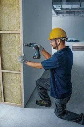 Worker installing drywall with CORDLESSS SCREW DRIVER GTB185-LI. Construction and building trades.